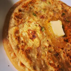 A close-up shot of the Aloo Paratha, with butter melting into the crispy, flaky layers. It's the ultimate comfort food.