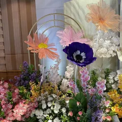 A close-up of the floral arrangement, showing the mix of fresh flowers and large, handcrafted paper flowers in vibrant colors. Golden arches add a touch of modern elegance.
