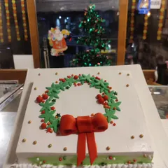 An elegant Christmas wreath cake. This square cake is decorated with a buttercream wreath, holly berries, and a red bow.
