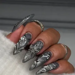 A closer look at the detail in this sculpted silver set. Each nail features a unique, hand-formed metallic design over a shimmering gunmetal base, creating a futuristic and edgy stiletto look.