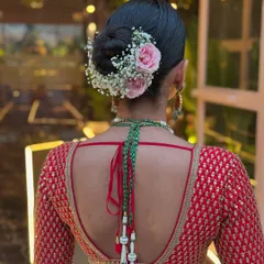 The perfect bridal bun from the back. This style features a clean, tight bun adorned with baby's breath and pink roses, a popular and elegant choice for modern brides.