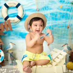 A perfect 'Beach Baby' theme, with this little one wearing a hat and sunglasses while sitting on a miniature beach chair. The set includes a nautical backdrop, a windmill, and seagulls.