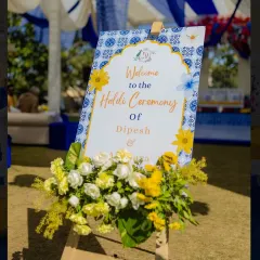 A close-up of the elegant welcome signage for the Haldi ceremony, framed with fresh yellow and white flowers.