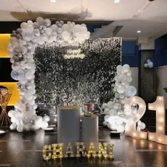 A stylish setup for a 21st birthday featuring a silver shimmer wall, a white and silver balloon arch, and large marquee numbers. The clean and modern look is perfect for milestone celebrations.