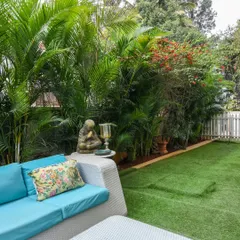 Here, I created a lush garden feel in a backyard using a comfortable wicker sofa set on a perfectly green artificial lawn. The space is surrounded by dense, natural foliage, with the artificial grass providing a clean, usable area for seating and relaxation.