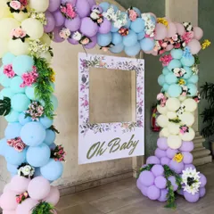 A beautiful "Oh Baby" photo frame surrounded by a pastel rainbow balloon arch. The arch is decorated with delicate flowers, making it perfect for a spring or garden-themed baby shower.