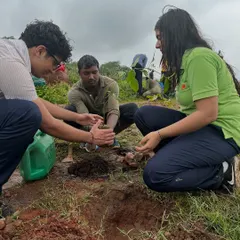 A student from The Shri Ram School gets guidance from our team member on how to properly plant a sapling during their drive at Aravali Nagar Van.