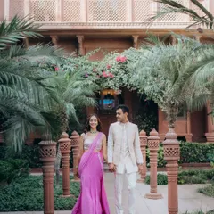 A classic walking shot of Kanav and Saloni in the courtyard of the Welcomhotel Khimsar. The symmetry of the architecture and the lush greenery create a regal and romantic setting.