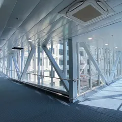 The interior of a glass skybridge connecting two blocks of Venkateshwar Hospital. The exposed structural trusses and floor-to-ceiling glass provide functional connectivity with unobstructed views.