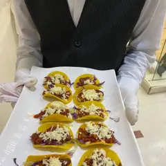 We bring global flavors to your party with our Mexican Tacos. These bite-sized tacos are filled with seasoned beans and vegetables, topped with fresh cheese, and served on a platter for easy enjoyment.
