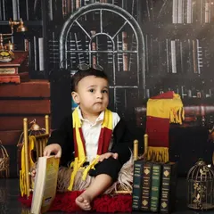 A moment of quiet contemplation for our little wizard. This pose shows off the full Gryffindor-style costume against the rich, dark library backdrop, perfect for a themed baby portrait.