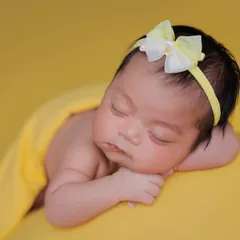 A close-up of a sleeping newborn against a bright yellow backdrop, showing the delicate details of their face.