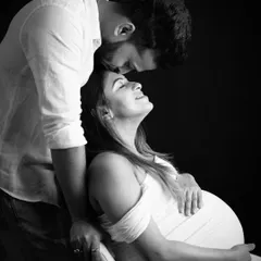 A tender black and white moment. The partner gently kisses the mom-to-be's forehead, creating a soft, romantic, and deeply emotional portrait.