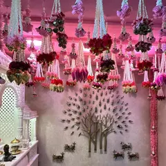 A full view of the room with the kalire-style floral ceiling. The pink lighting enhances the color of the flowers, and the decor beautifully frames the home's existing features, like the marble temple (mandir) and wall art.