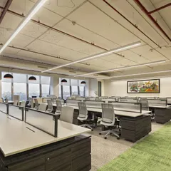 An open-plan work hall at the Carlsberg head office, featuring exposed ceilings with stenciled brand details. The design balances an industrial aesthetic with green carpeting and organized workstations to create a vibrant, collaborative atmosphere.