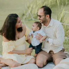 A family of three interacting during their outdoor session. The baby, dressed in a cute bow tie, looks inquisitively at his parents, creating a lovely candid moment.