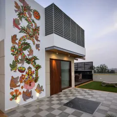 This terrace at the Kavyam Residence is a lively space for family gatherings. It blends tradition and modernity, featuring a vibrant Madhubani mural, a checkerboard stone floor, and a cozy seating area shaded by a wooden pergola.
