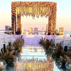 A picture of pure elegance. This seaside mandap, framed with lush florals and pampas grass, features a stunning mirror aisle that reflects the sky, creating a truly magical setting for your vows.