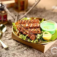 A wider view of the Mutton Adana Kebabs, presented on a wooden block with traditional lanterns in the background, creating a rustic and authentic vibe.