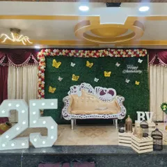 For grand milestone celebrations like a 25th anniversary, I design impressive stage setups. This features giant light-up marquee numbers, a lush green wall backdrop for photos, and an ornate sofa, turning any venue into a spectacular party space.