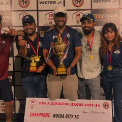 The entire management and coaching staff celebrating with the DSA A Division League trophy. This victory was a total team effort, on and off the pitch.
