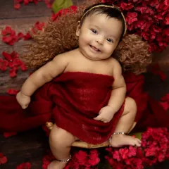 A sweet, gummy smile from a happy baby nestled in soft red wraps. The rich color and floral accents create a beautiful and warm portrait.
