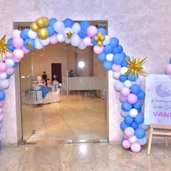 A beautiful balloon arch in pink, blue, white, and gold at the entrance, complete with star accents and a personalized welcome sign for baby Vani.