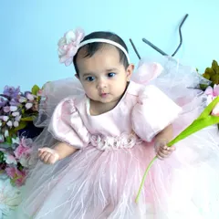 A close-up of a baby girl in a beautiful pink dress, holding a flower and looking curiously at the camera. We focus on capturing these quiet, observant moments during our sessions.