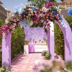The entrance to the pastel Mehendi, featuring a lilac archway adorned with a lush arrangement of pastel-colored flowers. The path leads to a memory station, setting a personal and sweet tone.