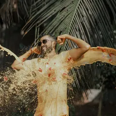 Capturing the pure, unadulterated fun of a Haldi ceremony. This high-energy shot freezes the moment the groom is joyfully drenched in turmeric paste and flower petals against a backdrop of lush palm leaves.