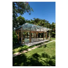 A daytime view of the glass pavilion, where the transparent roof and walls capture the dynamic play of sunlight and shadows from the overhead tree canopy. This space offers an immersive experience of being in the garden while sheltered from the elements.
