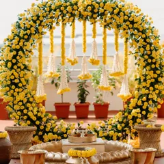 A beautiful and minimal Haldi setup with a full arch of yellow chrysanthemums and hanging floral tassels, perfect for intimate ceremonies.
