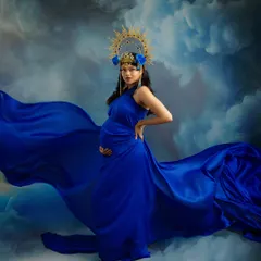 A bold and confident pose. This portrait captures the phenomenal power of a pregnant woman, with the rich blue gown and dramatic sky creating an unforgettable, artistic statement.