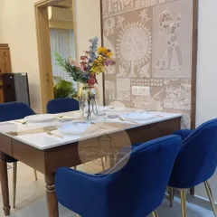 This dining area features a stunning custom wallpaper that acts as a piece of art. The solid wood dining table is paired with royal blue velvet chairs, creating an elegant space for meals and gatherings.
