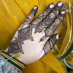 A striking geometric design on the back of the hand, using diamond shapes and clean lines for a very modern and chic look. The yellow background makes the dark henna lines stand out beautifully.