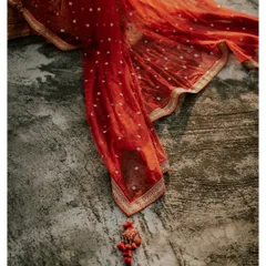 An artistic flat-lay of the bride's red dupatta, showcasing its delicate embroidery and tassels against a textured background.