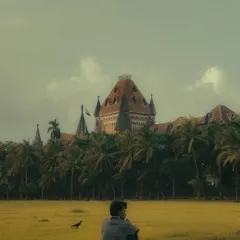 A young man sits alone in the vast green expanse of Oval Maidan, with the Bombay High Court in the background. This image captures a powerful sense of solitude and introspection within a public space.