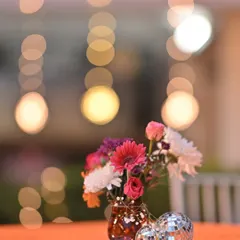 We use lighting and decor to set the mood. This artistic shot captures a colorful floral arrangement and mini disco balls, with the soft bokeh of party lights in the background, hinting at a fun-filled Sangeet night.