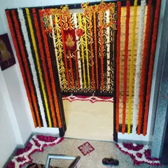 This is a complete entrance decoration for a puja at home. It features hanging marigold garlands and a floor rangoli made of flower petals to welcome guests.
