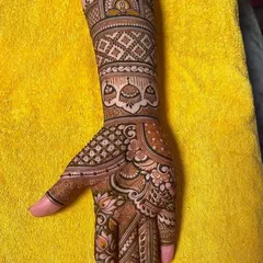 A close-up of a hand with a traditional Indian mehndi design, featuring bells and checkerboard patterns.