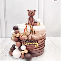 A chic and modern baby shower cake with a cascade of brown and white chocolate spheres. The cute fondant teddy bear on top adds a touch of sweetness.