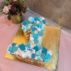 A first birthday monogram cake for a baby boy. This number "1" is decorated with blue frosting, chocolate buttons, and other sweet treats.
