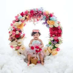 A happy baby girl sits inside a beautiful ring of flowers, holding a small bouquet and smiling brightly for her portrait.