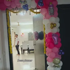 The entrance to a home decorated for a baby girl's welcome. The pink, white, and gold balloon arch is accented with baby-themed foil balloons and traditional marigold garlands for a festive touch.
