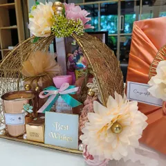 A beautiful wedding hamper in a golden wire basket, filled with a scented candle, Ferrero Rocher, and other goodies. The peach and cream floral theme adds a soft, romantic touch.