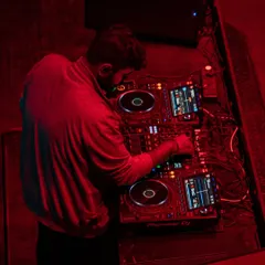 An overhead shot from a live DJ set, captured in the middle of the mix. The red lighting and focused atmosphere show the intensity of a club performance.
