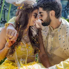 An intimate Haldi moment. The couple, covered in yellow petals, share a quiet, loving glance, showing that even in the midst of celebration, there are moments of pure connection.
