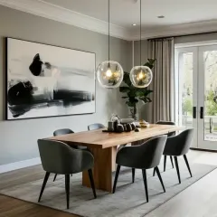This dining room design achieves a perfect balance of modern minimalism and warmth. A solid wood table is paired with contemporary grey chairs, set under two simple glass pendant lights, while a large abstract painting adds a dramatic touch.