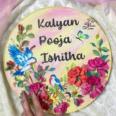 This circular nameplate is a celebration of family, featuring three names and adorned with sculpted birds and roses. The soft pink and yellow background adds a warm and welcoming touch.