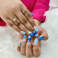 Catch the waves of style with these dreamy beach shell nails. This set features a stunning blue marble effect, glitter, and crystal accents for a look inspired by the ocean.